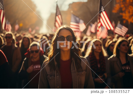 Beautiful young girl against the backdrop of huge crowd of people marching along a city street with American flags. Stars and Stripes flutter over people's heads. Independence Day 4th of July concept. 108535527