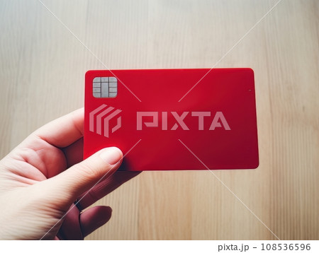 Female hand holding a red bank card on a wooden table background AI Female hand holding a red bank card on a wooden table background AI 108536596