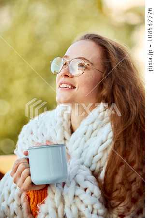 Close up portrait of enjoying and inspired young beautiful girl covered with blanket and drinking warm hot cup of coffee, tea, chocolate. Close up portrait of enjoying and inspired young beautiful girl covered with blanket and drinking warm hot cup of coffee, tea, chocolate. 108537776