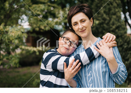 Mom with teenage son are walking in the park. They look at each other and smile. A woman hugs boy and straightens her hair. The concept of mother's day, relationships with adolescents, care and love. Mom with teenage son are walking in the park. They look at each other and smile. A woman hugs boy and straightens her hair. The concept of mother's day, relationships with adolescents, care and love. 108538251