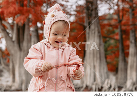 Cute child girl walking and playing in a autumnal forest. Little girl in warm clothes walks in the park Cute child girl walking and playing in a autumnal forest. Little girl in warm clothes walks in the park 108539770