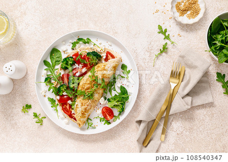 Omelette stuffed with tomato, broccoli, feta cheese and fresh green leaves of arugula and spinach. Healthy diet food, breakfast. Top view Omelette stuffed with tomato, broccoli, feta cheese and fresh green leaves of arugula and spinach. Healthy diet food, breakfast. Top view 108540347