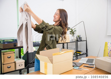 Asian young beautiful woman unboxing cardboard delivery package and holding with ordered clothes, Excited lady shopper unpack cardboard box with clothes, happy and smiling Asian young beautiful woman unboxing cardboard delivery package and holding with ordered clothes, Excited lady shopper unpack cardboard box with clothes, happy and smiling 108540856