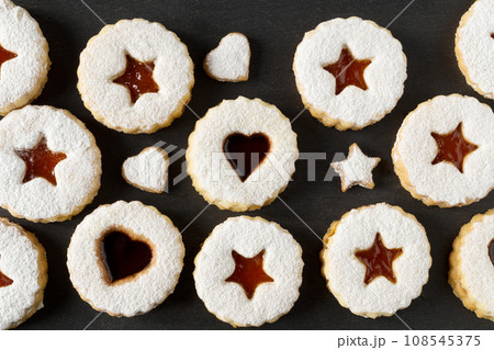 Linzer cookies with apricot jam sprinkled with powdered sugar on a black background. Festive dessert. Top view Linzer cookies with apricot jam sprinkled with powdered sugar on a black background. Festive dessert. Top view 108545375