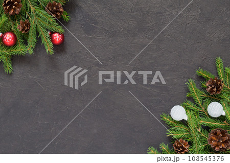 Christmas background with Christmas tree branches and balls decorations in red and white, dark textured background. New Year festive decor. Spruce pine cones. Top view with copy space, flat lay 108545376