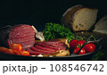 Whole and sliced bresaola on a metal round tray with tomatoes, garlic and bread 108546742