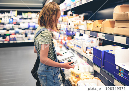 Pretty girl child choosing yogurt in supermarket. Beautiful female preteen kid looking milk products in grocery store Pretty girl child choosing yogurt in supermarket. Beautiful female preteen kid looking milk products in grocery store 108549573