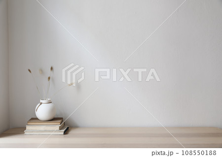 Elegant Scandinavian interior. White ball vase with dry grass, lagurus bouquet on old books. Empty wall background. Modern living room, home office. Minimal moody autumn decor in cozy apartment. 108550188