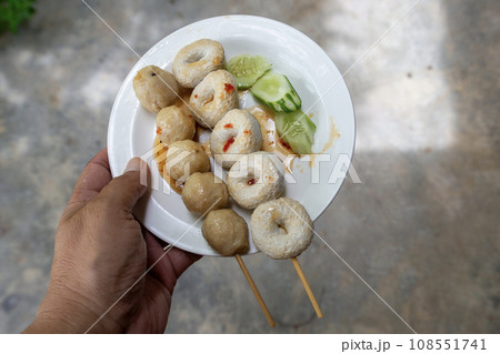 Someone's hand holding a white plate of pork balls and fish balls each. Someone's hand holding a white plate of pork balls and fish balls each. 108551741