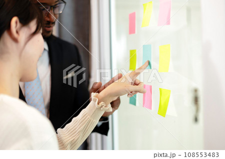 Happy multiethnic business team meeting pointing at post it notes on glass board. Happy multiethnic business team meeting pointing at post it notes on glass board. 108553483