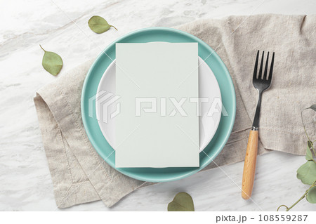 Green blank menu card mockup on plate with fork on linen napkin on marble table, top view 108559287