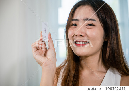 Close up woman showing rapid antigen test kit for selftest with Negative result during swab COVID-19 testing, female holding perform fast coronavirus ATK self test at home in living room, nasal Close up woman showing rapid antigen test kit for selftest with Negative result during swab COVID-19 testing, female holding perform fast coronavirus ATK self test at home in living room, nasal 108562831