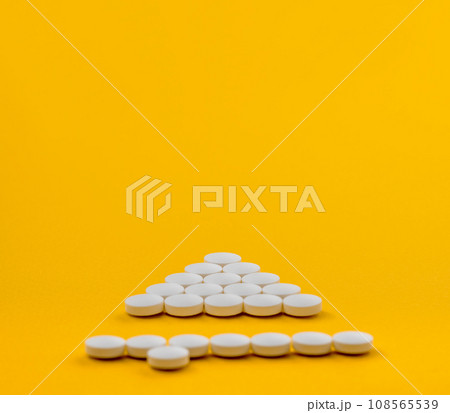 White medical pills in shape of upwards arrow on yellow background. Medicine, pills background. Treatment. Prevention. 108565539