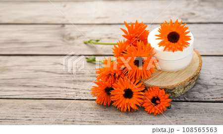 Cream for body care with calendula. Cosmetic cream for cleansing the skin with calendula flowers. Medical Dermatology. Fresh orange calendula flowers on a wooden background in nature. 108565563