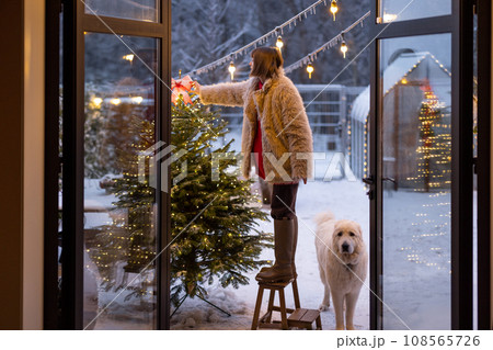 Woman decorates Christmas tree on house terrace outdoors 108565726