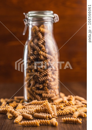 Raw whole grain fusilli pasta. Uncooked pasta in jar on wooden table. Raw whole grain fusilli pasta. Uncooked pasta in jar on wooden table. 108566061
