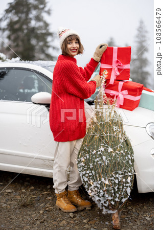 Woman with wrapped Christmas tree and presents near car in mountains 108566479