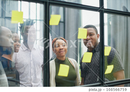 a team of young designers sticking notes on glass in a modern office a team of young designers sticking notes on glass in a modern office 108566759