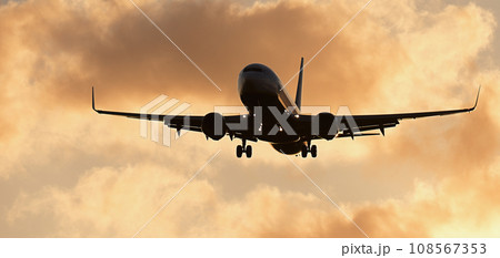 Silhouette passenger airplane. Front of silhouette airplane is flying in the orange sky with clouds, Passenger aircraft is landing. Commercial plane 108567353