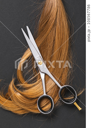 Top view of scissors and a cut off strand of children's blond hair on a dark paper background Top view of scissors and a cut off strand of children's blond hair on a dark paper background 108567786