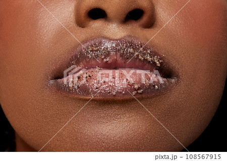 Closeup view of African-American woman with lips covered in sugar. Exfoliate spa treatment for lips. 108567915