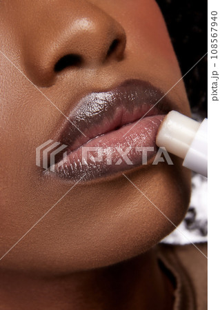 Perfect natural lip makeup. Close up photo of African-American woman applying hygienic lip balm. Moisturizing chap stick for dry lips. 108567940