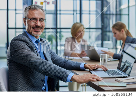 Happy businessman wearing eyeglasses sitting with laptop Happy businessman wearing eyeglasses sitting with laptop 108568134