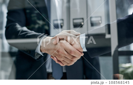 executives shaking hands in front of their manager and a colleague 108568145