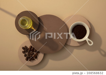 Top view of dark and light brown podiums decorated on brown background with coffee beans, coffee powder and glass jar of oil. Blank space for display product Top view of dark and light brown podiums decorated on brown background with coffee beans, coffee powder and glass jar of oil. Blank space for display product 108568632