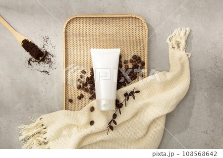 Abstract background for branding and minimal presentation cosmetic with ingredient from coffee. A white plastic tube with coffee beans on bamboo tray and beige cloth decorated on cement background 108568642