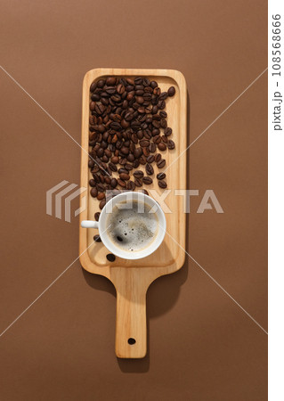 Against the brown background, a delicious cup of espresso decorated with coffee beans on wooden cutting board. Scene for advertising drinking product with minimal concept Against the brown background, a delicious cup of espresso decorated with coffee beans on wooden cutting board. Scene for advertising drinking product with minimal concept 108568666