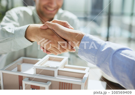 handshake against the background of a model of a house under construction. client and designer handshake against the background of a model of a house under construction. client and designer 108569409