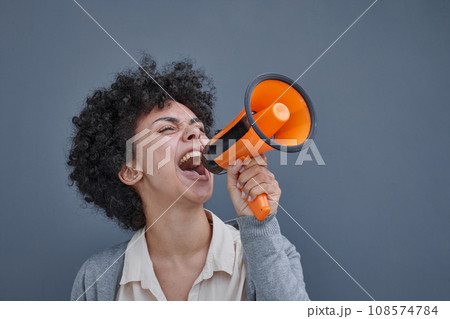 a girl on a gray background holds a loudspeaker in her hand. screams 108574784