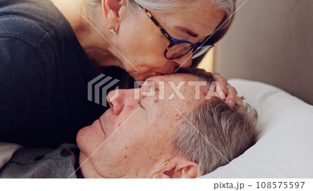 Senior woman kissing her husband on forehead with love, care and marriage in bed at home. Sick, recovery and elderly couple in retirement with illness in bedroom of hospice, nursing center or house. Senior woman kissing her husband on forehead with love, care and marriage in bed at home. Sick, recovery and elderly couple in retirement with illness in bedroom of hospice, nursing center or house. 108575597