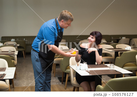 Male waiter brings orange juice to client Male waiter brings orange juice to client 108576127
