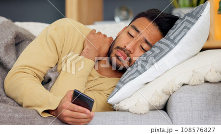 Man, phone and blanket on sofa in home living room, tired and web chat with email notification. Guy, smartphone and sick with research for health, medicine and watch video on social media in house 108576827