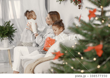 People reparing for Christmas. Mother playing with her daughters. Family is resting in a festive room. Child in a sweater sweater. 108577350
