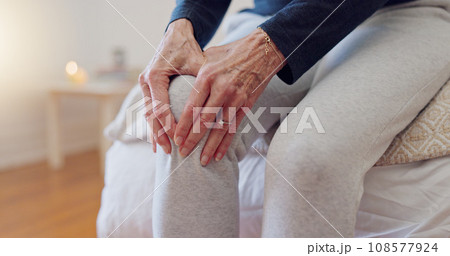 Hands, pain and closeup of senior woman in bedroom with injury, hurt or accident at nursing home. Sick, illness and zoom of elderly female person in retirement holding leg with sprain muscle at house 108577924