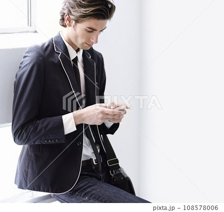 Fashion, phone and young man networking on social media, mobile app or the internet with formal outfit. Chat, communication and male person scroll on a cellphone with classy, cool and elegant style. 108578006