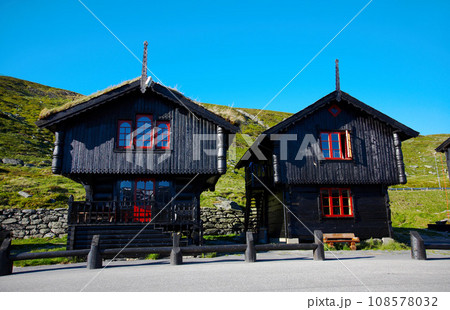 Houses, wood cabin and cottage in countryside outdoor, building and architecture over blue sky in summer at garden, grass and landscape. Chalet, home exterior and nature, road and street in Norway 108578032