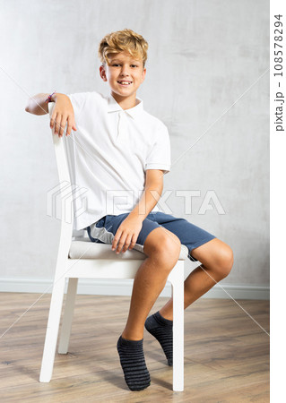Positive boy in casual clothes posing while sitting on chair Positive boy in casual clothes posing while sitting on chair 108578294