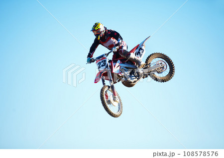 Person, motorcycle and jump adventure in blue sky as professional in action, competition or fearless. Bike rider, off road race or air stunt for speed driving at rally, extreme sport or challenge Person, motorcycle and jump adventure in blue sky as professional in action, competition or fearless. Bike rider, off road race or air stunt for speed driving at rally, extreme sport or challenge 108578576