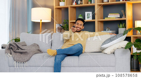 Watching tv, streaming and subscription with a man on a sofa in the living room of his home to relax. Television, video and remote with a young person changing the movie channel in his apartment 108578658