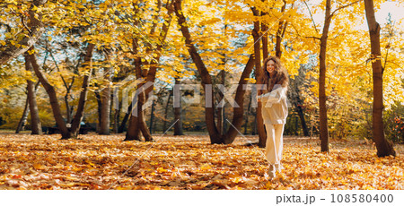 Smiling running woman plays and jumping dancing in the autumn forest with the yellow leaves at sunset. Copy space. Smiling running woman plays and jumping dancing in the autumn forest with the yellow leaves at sunset. Copy space. 108580400