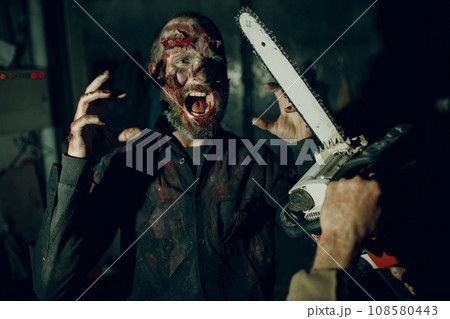 Walking dead zombie and chainsaw attack on horror halloween party. Walking dead zombie and chainsaw attack on horror halloween party. 108580443