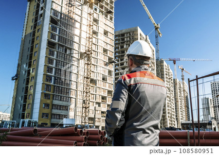 Builder at a construction site. Construction of a high-rise building and a builder looking at the process Builder at a construction site. Construction of a high-rise building and a builder looking at the process 108580951