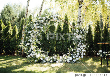 Circle wedding arch decorated with white flowers and greenery outdoors. 108583613