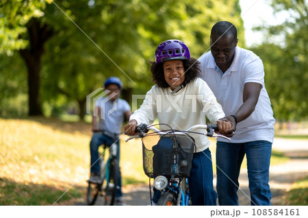 Happy dad teaching his kids to ride a bike Happy dad teaching his kids to ride a bike 108584161
