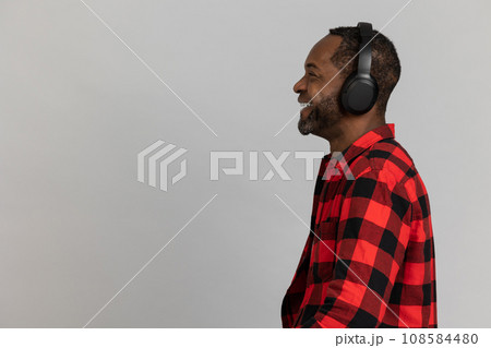 Profile of happy black bearded man in headphones wearing red checkered shirt listening to music Profile of happy black bearded man in headphones wearing red checkered shirt listening to music 108584480