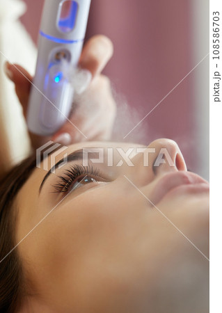 cosmetologist using primer spray for eyelash extension procedure in salon 108586703